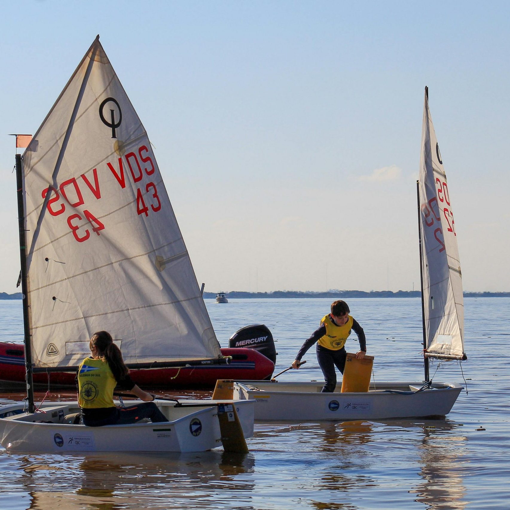 Children sailing small boats on a calm sea under a clear sky, enjoying watersports.